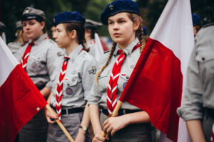 ZHP upamiętni 80. rocznicę Powstania Warszawskiego ogólnopolską kampanią 1 ZHP upamiętni 80. rocznicę Powstania Warszawskiego. Na zdjęciu znajdują się harcerki w mundurach ZHP trzymające biało-czerwone flagi Polski.
