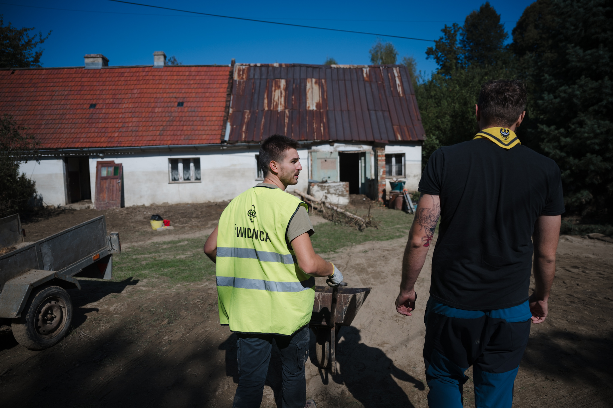 Pomoc dla powodzian - na zdjęciu harcerz w kamizelce odblaskowej, pchający taczkę na podwórku