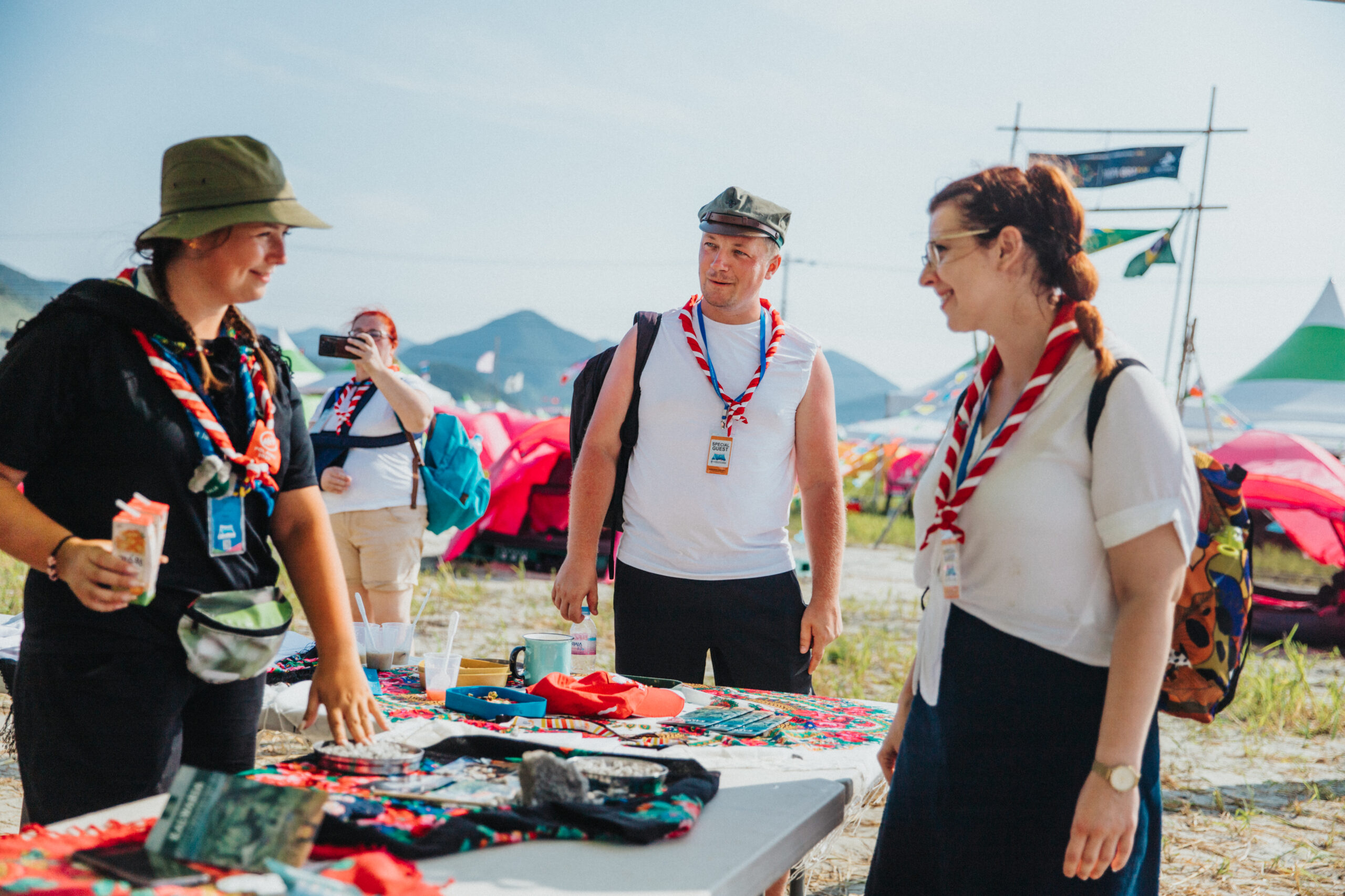 International Service Team - skauci z założonymi chustami stoją przy stoisku i rozmwaiają.
