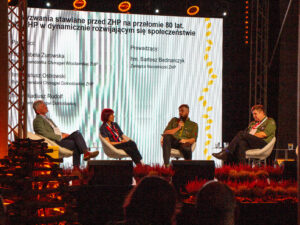 Tradycja, służba i kompetencje na całe życie. Kongres 80-lecia ZHP na Dolnym Śląsku 3 Instruktorzy ZHP i osoby zaproszone prowadzące panel, w tle biały ekran z prezentacją multimedialną.