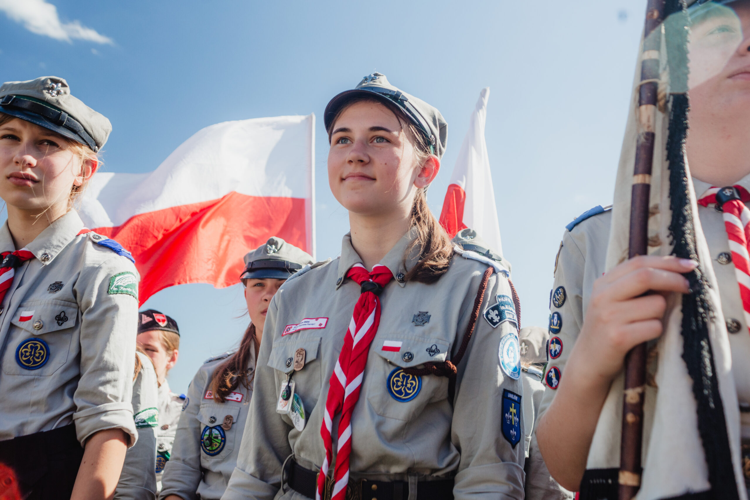 Patriotyzm może być radosny - radosna harcerka w mundurze, w tle flagi biało-czerwone.